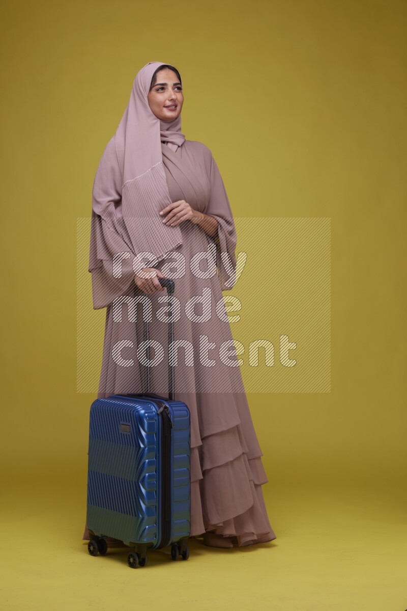 A woman With suit Case on a Yellow Background wearing Brown Abaya with Hijab