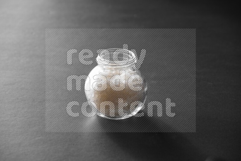 A glass spice jar full of salt on black flooring