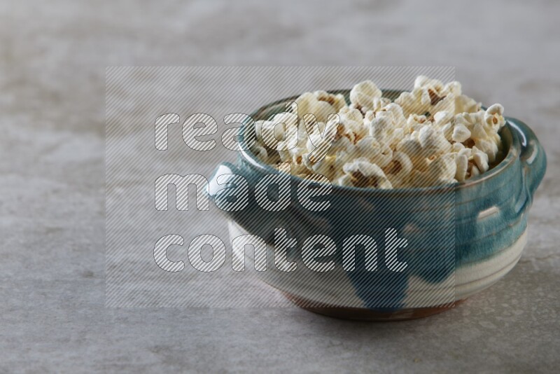 popcorn in a multi-colored handheld ceramic bowl on a grey textured countertop