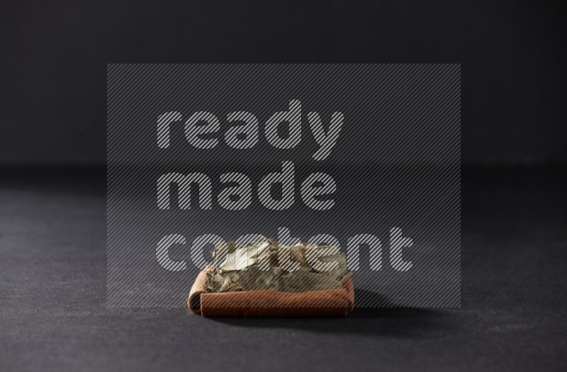 أربعة من أعواد القرفة مكونة شكل مربع بداخلها أوراق الغار علي خلفية سوداء