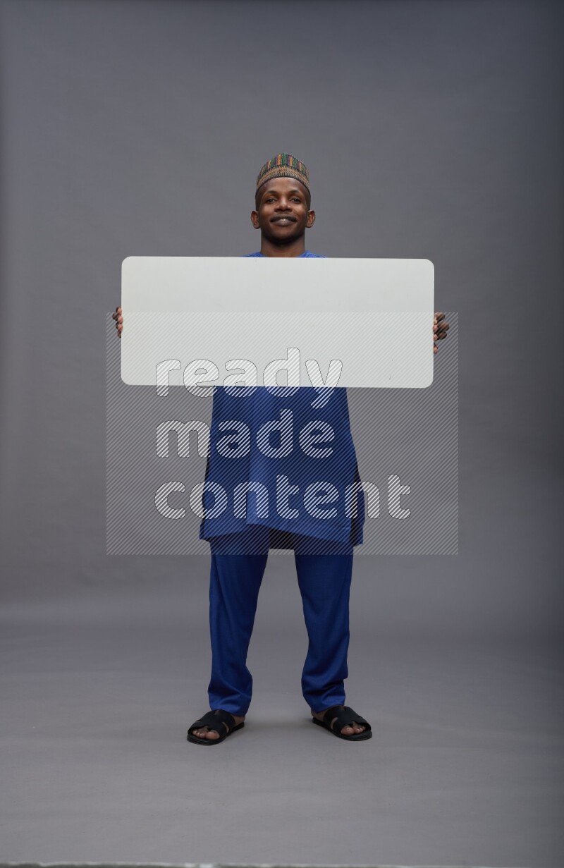 Man wearing Nigerian outfit standing holding board on gray background