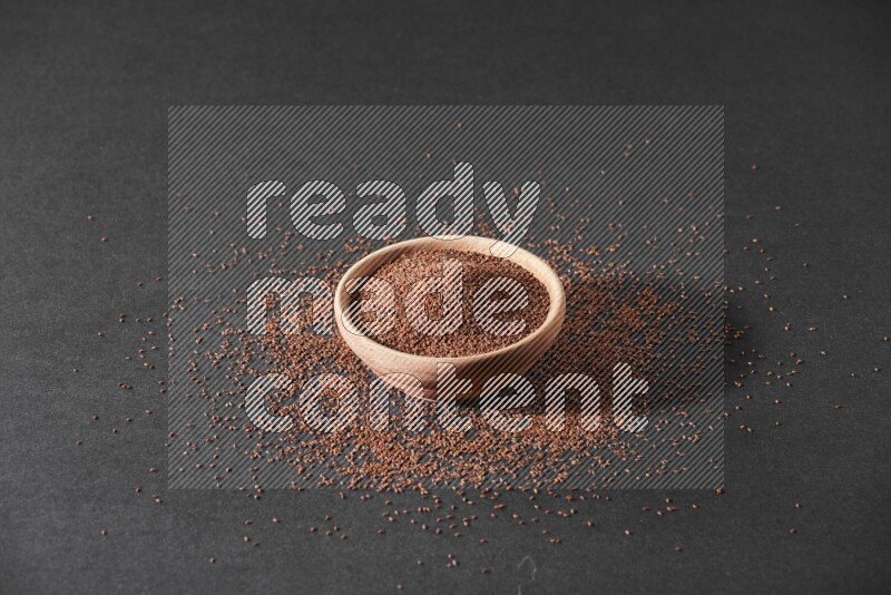 وعاء خشبي ممتلئ ببذور حب الرشاد محاط ببعض البذور علي خلفية سوداء