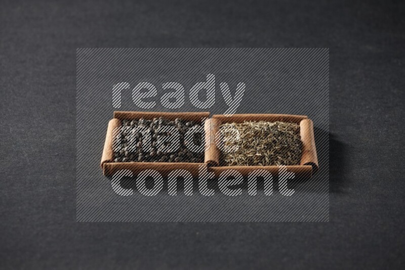 مربعان من أعواد القرفة ممتلئان بحبوب الفلفل الأسود وحبوب الكمون علي خلفية سوداء