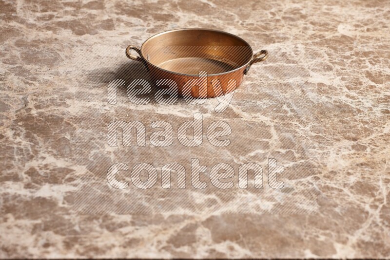 A small copper pan on beige marble background
