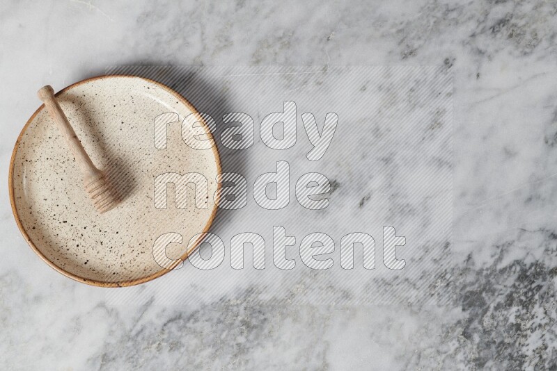 Beige pottery plate with wooden honey dipper in it on grey marble background