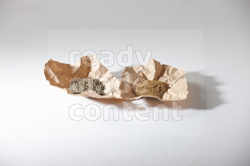 Cumin seeds and cumin powder in 2 crumpled pieces of paper on white flooring