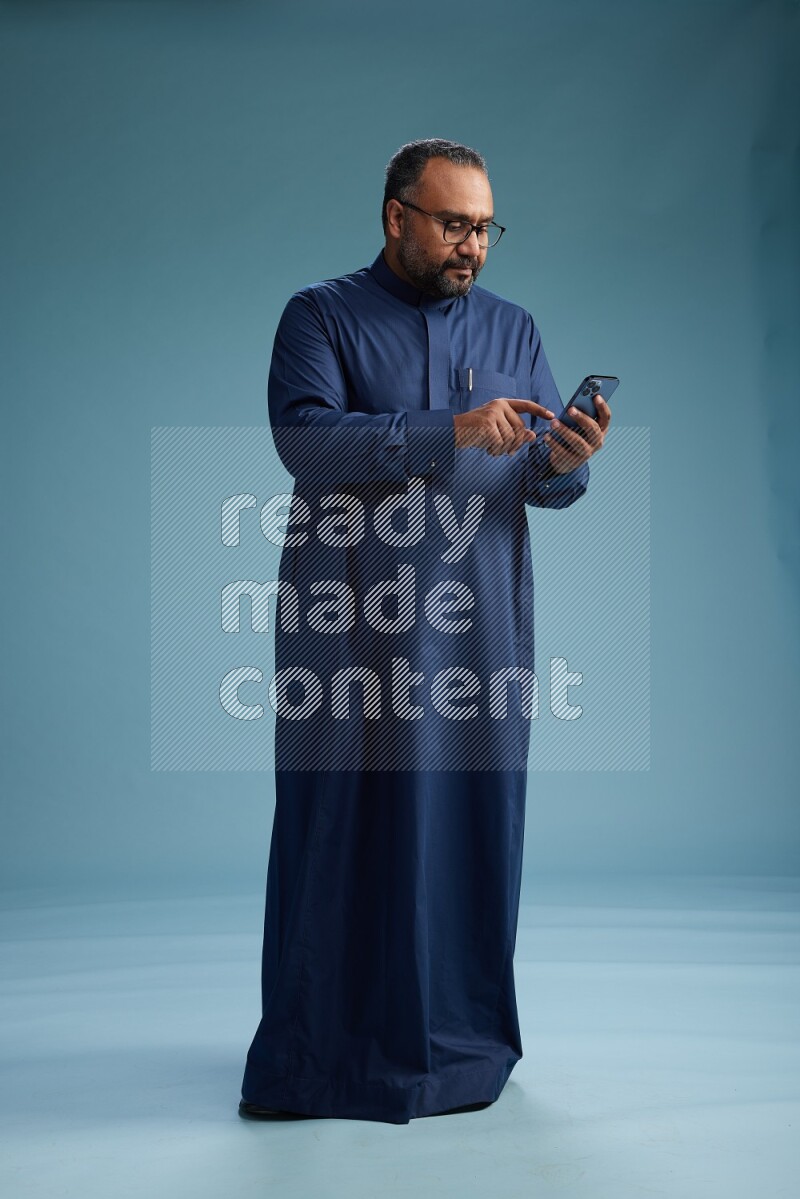 Saudi Man without shimag Standing texting on phone on blue background