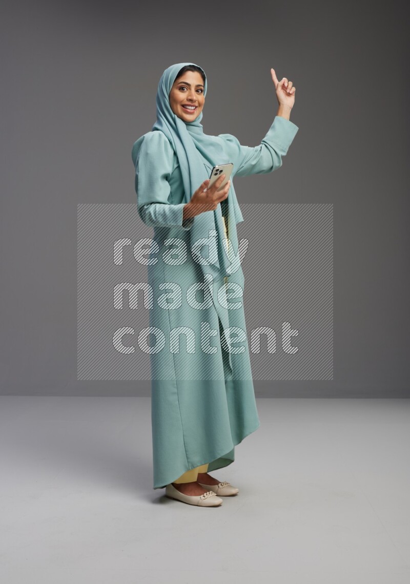 Saudi Woman wearing Abaya standing texting on phone on Gray background