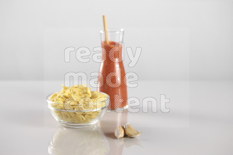 Raw pasta with tomatoe pasta with different ingredients such as cherry tomatoes, basil, garlic, bay laurel, cardamom, white pepper, black pepper, red chilis and wheat stalks on light grey background