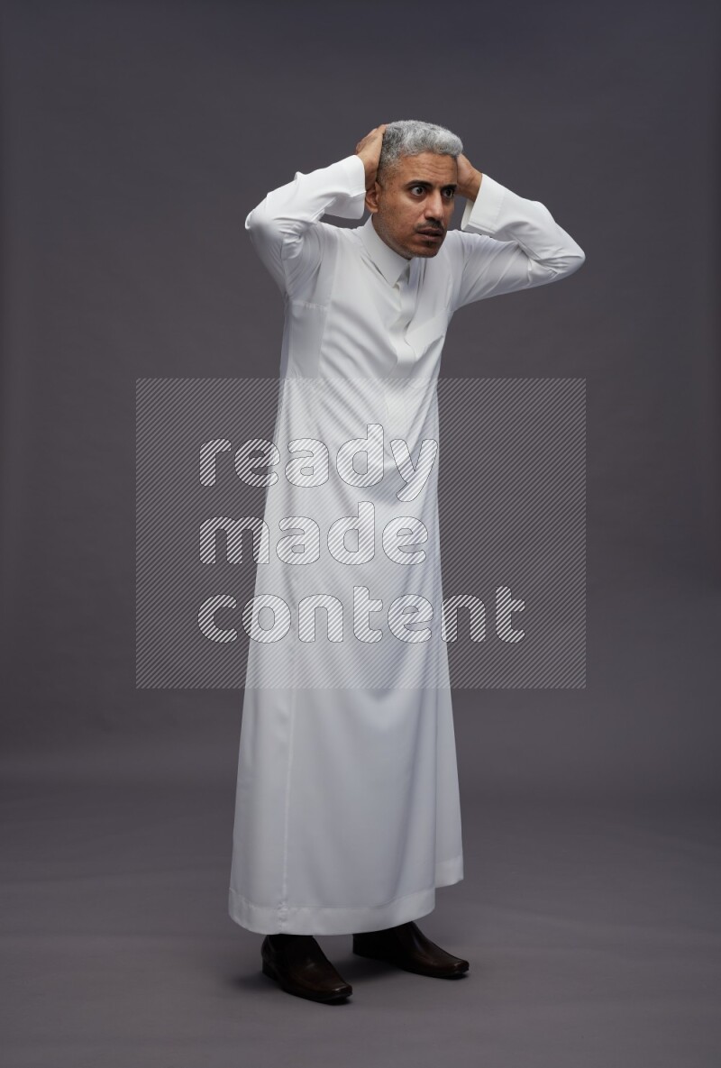 Saudi man wearing thob standing hands behind head on gray background