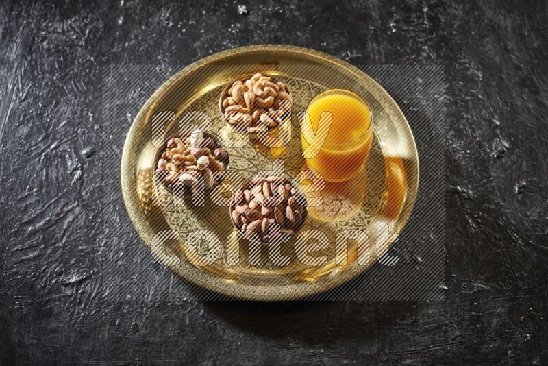 Nuts in metal bowls with qamar eldin on a tray in dark setup
