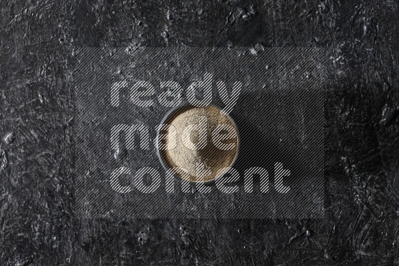 وعاء فخار أسود مملوء ببودرة الفلفل الأبيض على أرضية سوداء