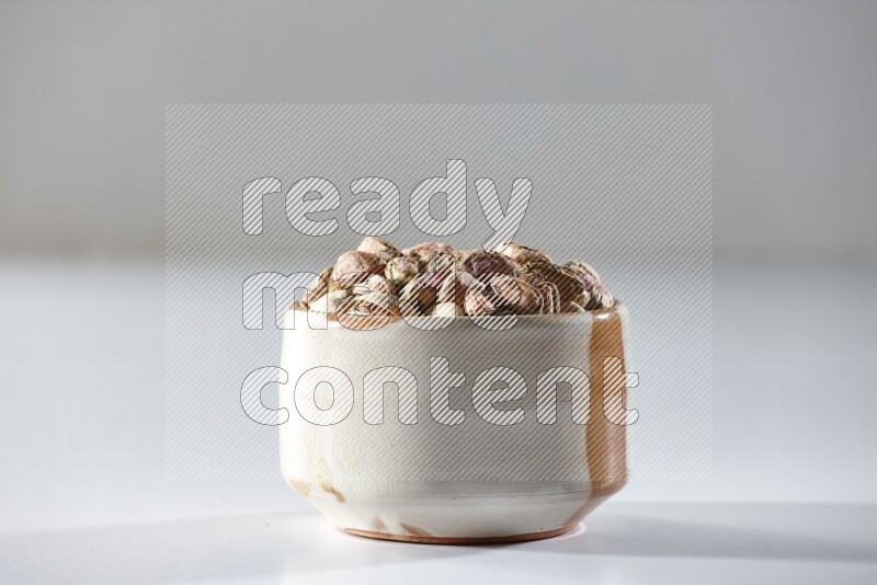 A beige ceramic bowl full of peeled pistachios on a white background in different angles