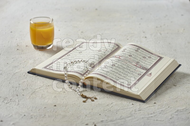 Quran with dates, prayer beads and different drinks all placed on textured white background