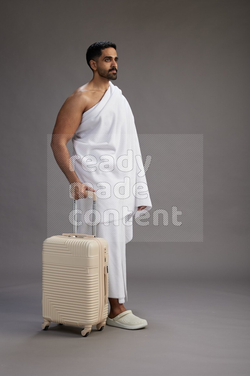 A man wearing Ehram Standing holding traveling bag on gray background