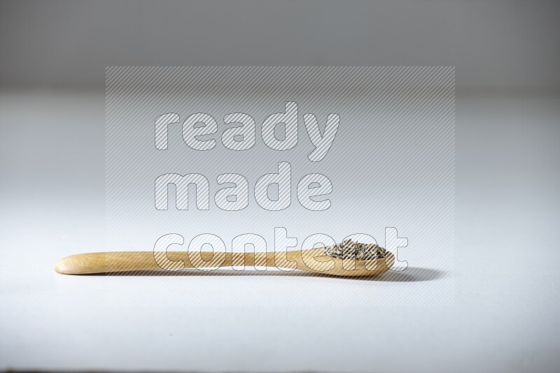 A wooden spoon full of cumin seeds on a white flooring