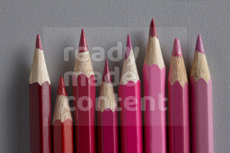 A collection of colored pencils arranged showcasing a gradient of pink and red hues on grey background