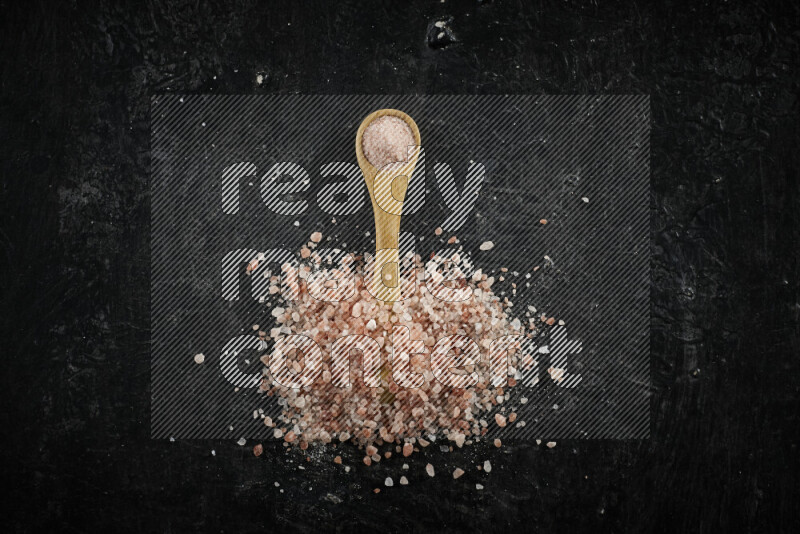 A wooden spoon full of pink himalayan salt on black background
