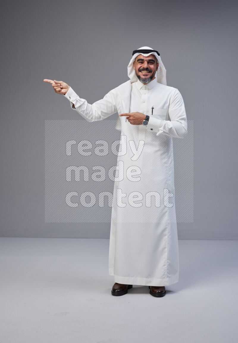 Saudi man Wearing Thob and white Shomag standing interacting with the camera on Gray background