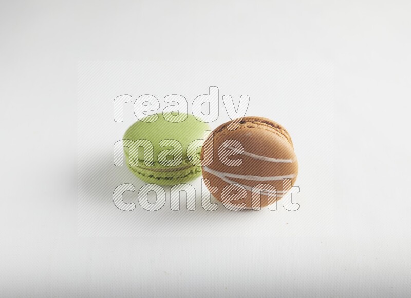 45º Shot of of two assorted Brown Irish Cream, and Green Pistachio macarons on white background