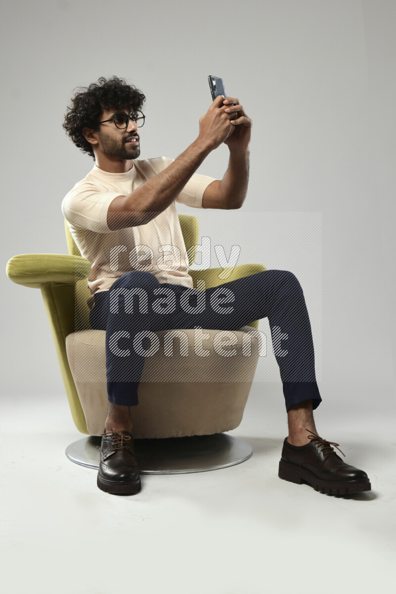 A man wearing casual sitting on a chair taking a selfie on white background