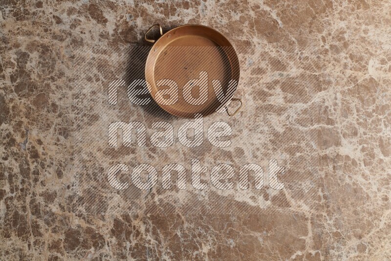 A small copper pan on beige marble background