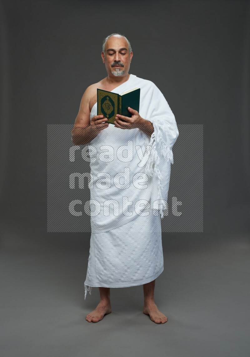 A man wearing Ehram Standing reading quran on gray background