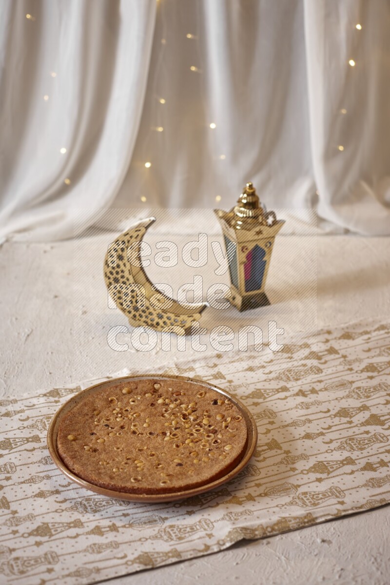 صحن من البسبوسة بجانب فوانيس علي خلفية بيضاء خشبية