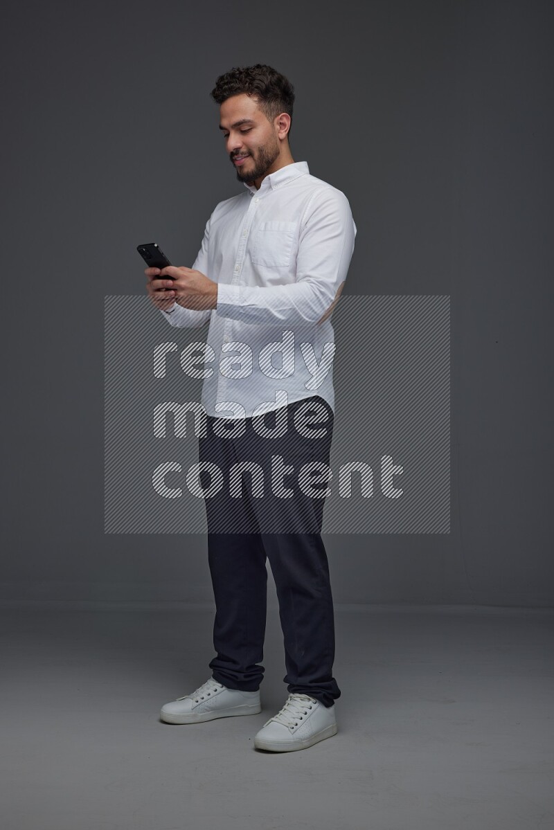 A man wearing smart casual standing and using his phone eye level on a gray background