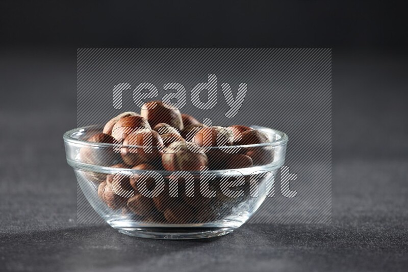 A glass bowl full of hazelnuts on a black background in different angles