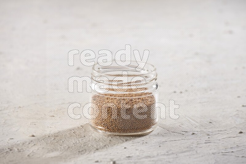 A glass jar full of mustard seeds on a textured white flooring