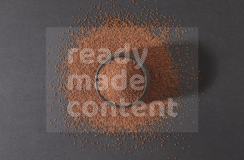 A black pottery bowl full of garden cress seeds surrounded by seeds on a black flooring