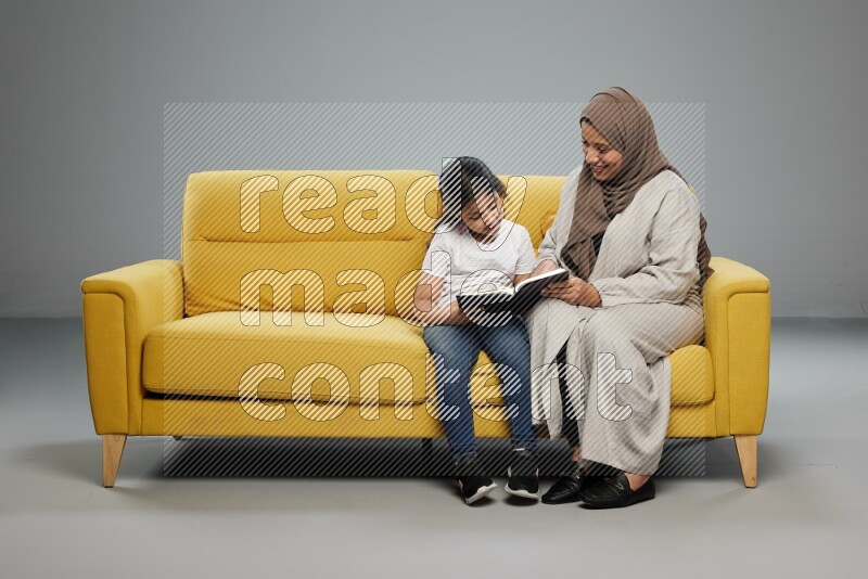 Mom and daughter sitting reading a book on gray background