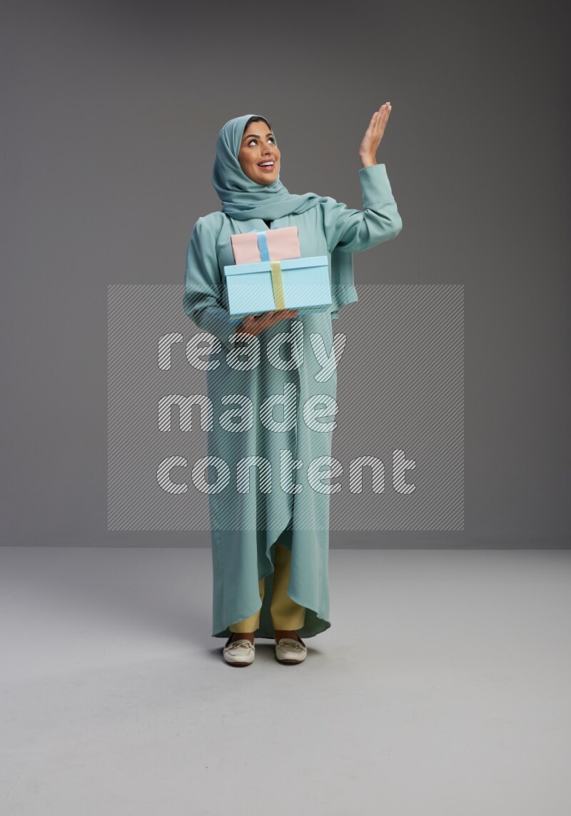 Saudi Woman wearing Abaya standing holding gift box on Gray background
