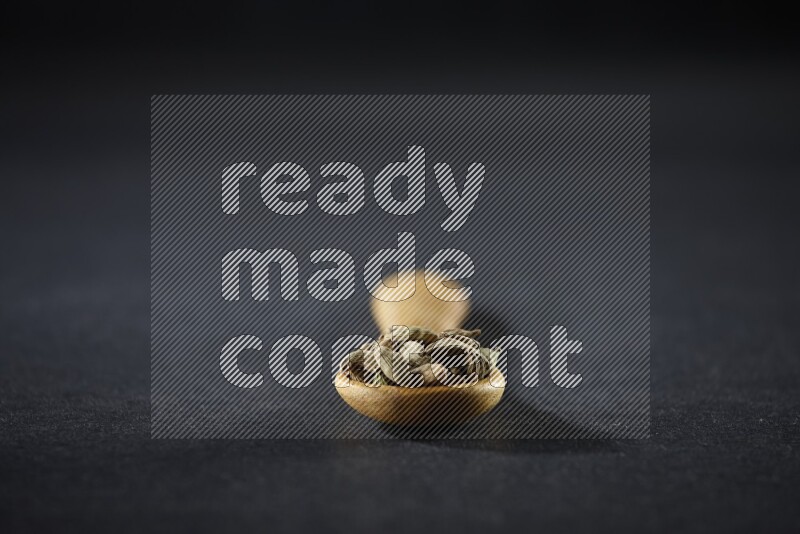 A wooden spoon full of cardamom on black flooring