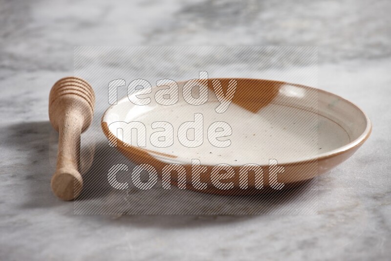 Multicolored pottery plate with wooden honey dipper on the side on grey marble background