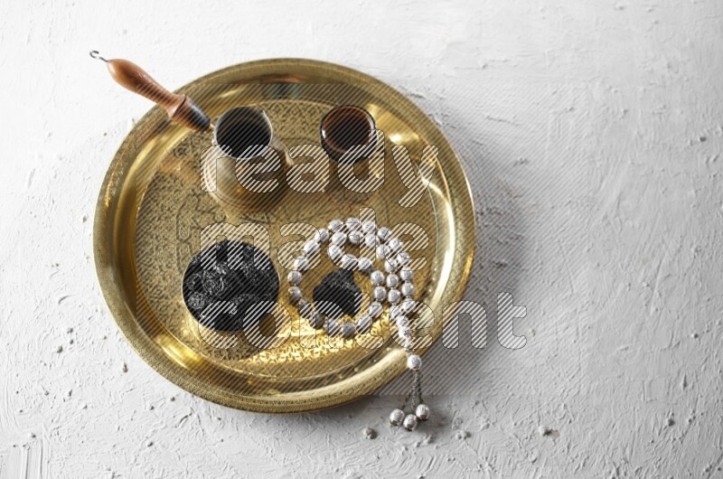 Dried plums in a metal bowl with coffee and prayer beads on a tray in a light setup