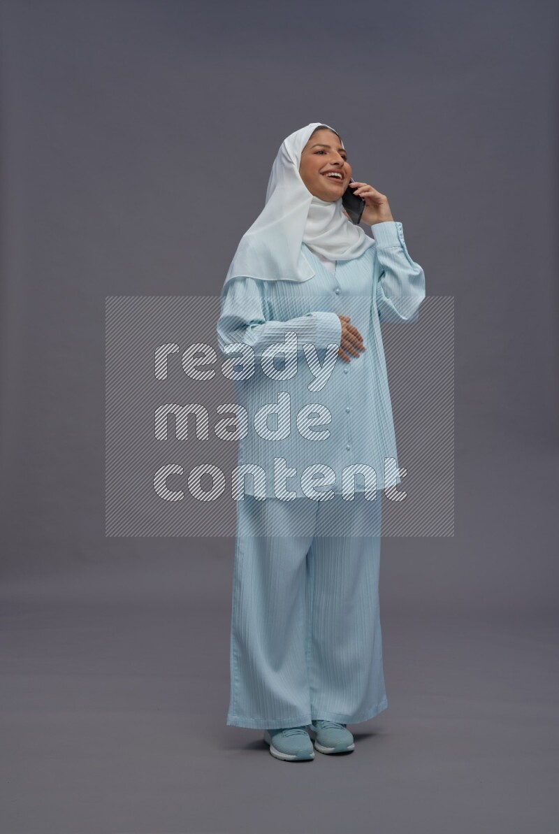 Saudi woman wearing hijab clothes standing talking on phone on gray background