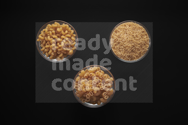 Different pasta types in glass bowls on black background