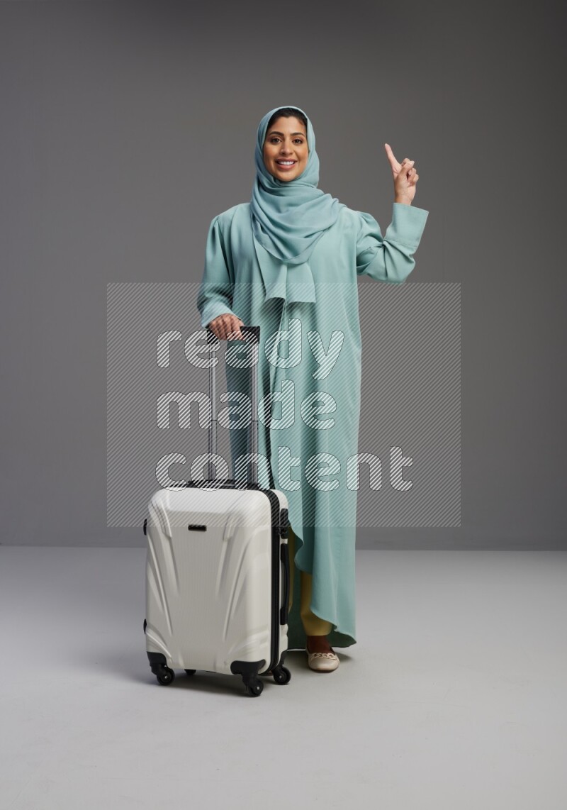 Saudi Woman wearing Abaya standing holding Travel bag on Gray background