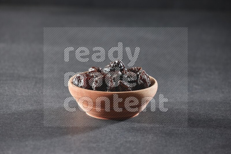 A wooden bowl full of dried plums on a black background in different angles
