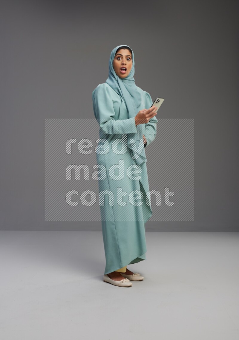 Saudi Woman wearing Abaya standing texting on phone on Gray background