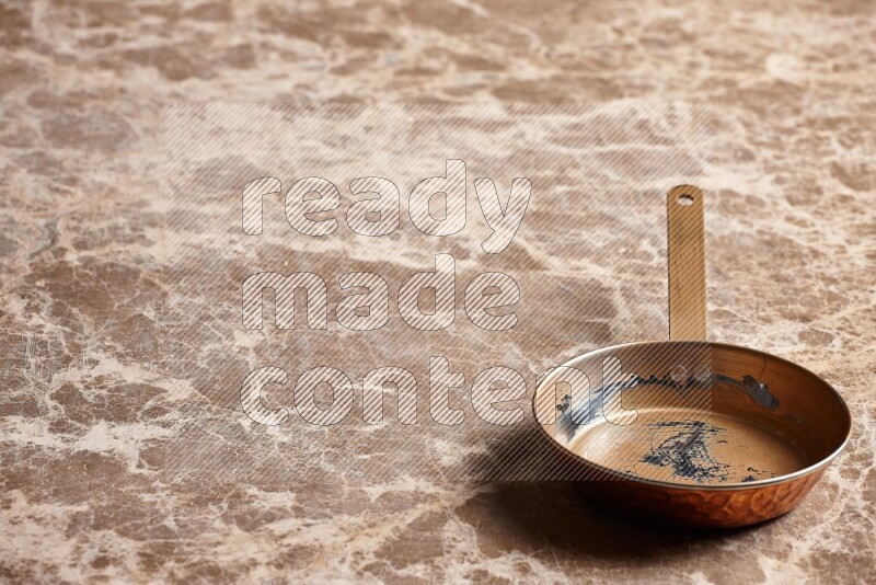A small copper pan on beige marble background