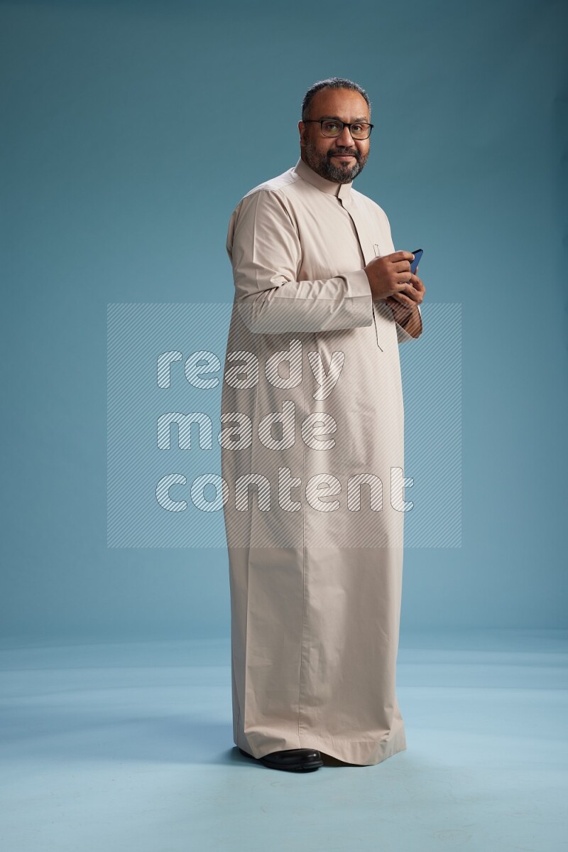Saudi Man without shimag Standing texting on phone on blue background