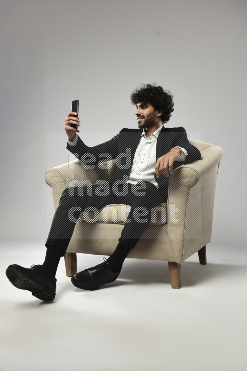 A man wearing formal sitting on a chair taking a selfie on white background