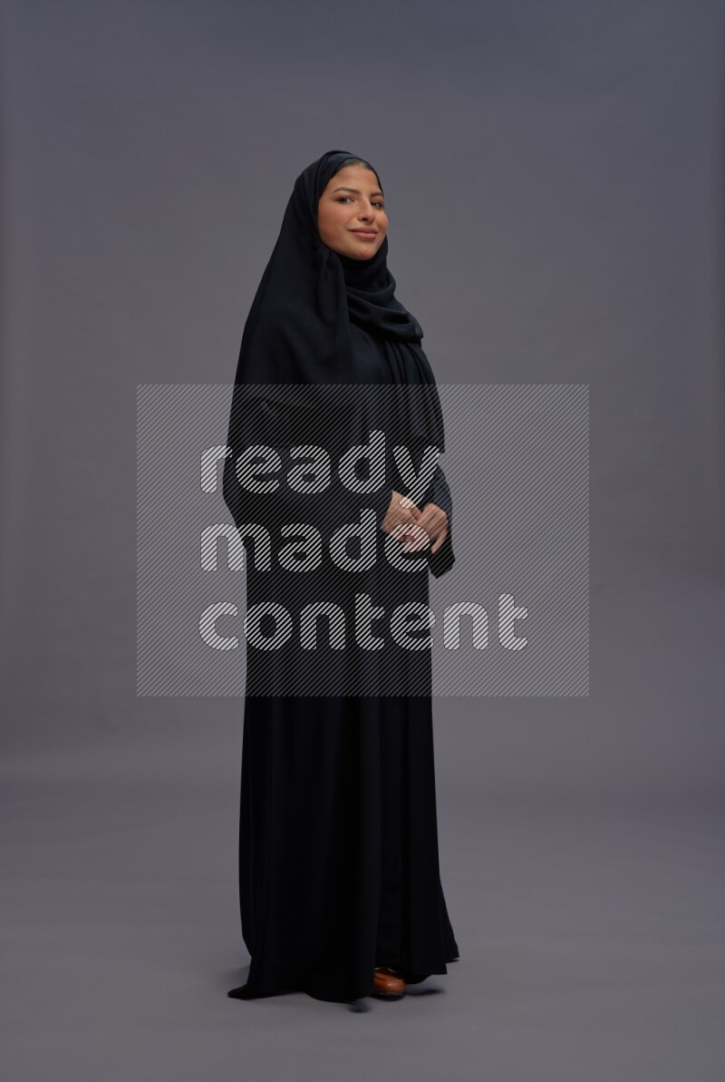 Saudi woman wearing Abaya standing interacting with the camera on gray background