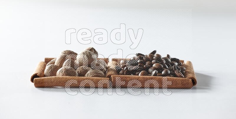 مربعان من أعواد القرفة ممتلئان بحبوب القهوة وجوزة الطيب علي خلفية بيضاء