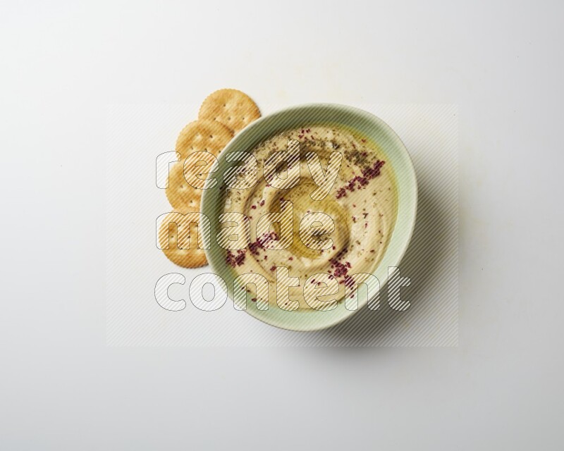 Hummus in a green plate garnished with zattar & sumak on a white background