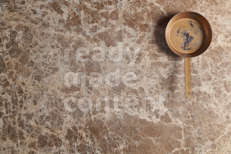 A small copper pan on beige marble background