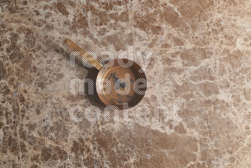 A small copper pan on beige marble background